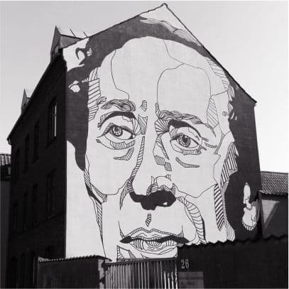 A large line drawn mural of a moustached face covering the gable end of a brick building