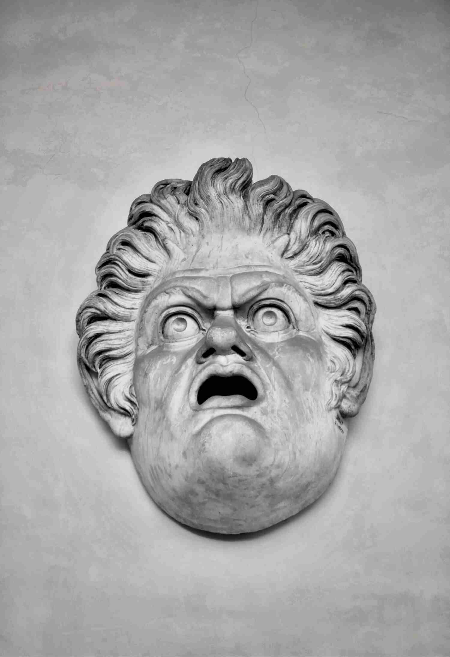 A carved stone theatrical mask with an open mouth and wild hair