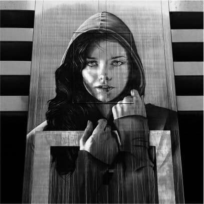 A large monochrome mural of a woman in a hooded coat painted across a concrete building facade