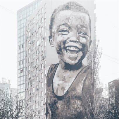A vast mural of a smiling child painted across the side of a residential tower block