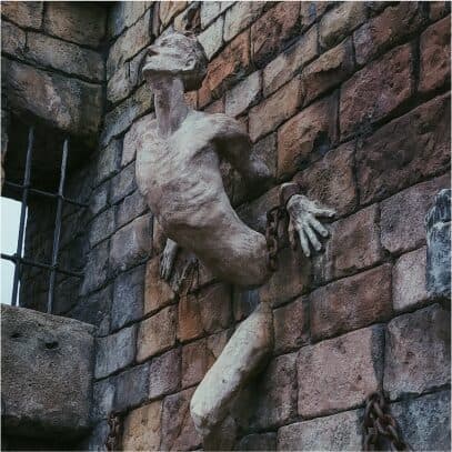 A pale sculpted figure mounted on a weathered stone wall beside iron chains