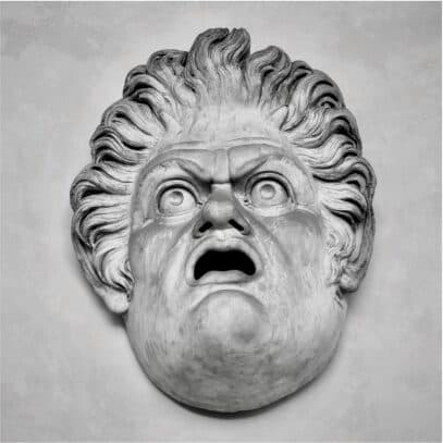 A carved stone theatrical mask with an open mouth and wild hair
