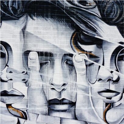 A grey mural of overlapping faces and hands painted on brickwork